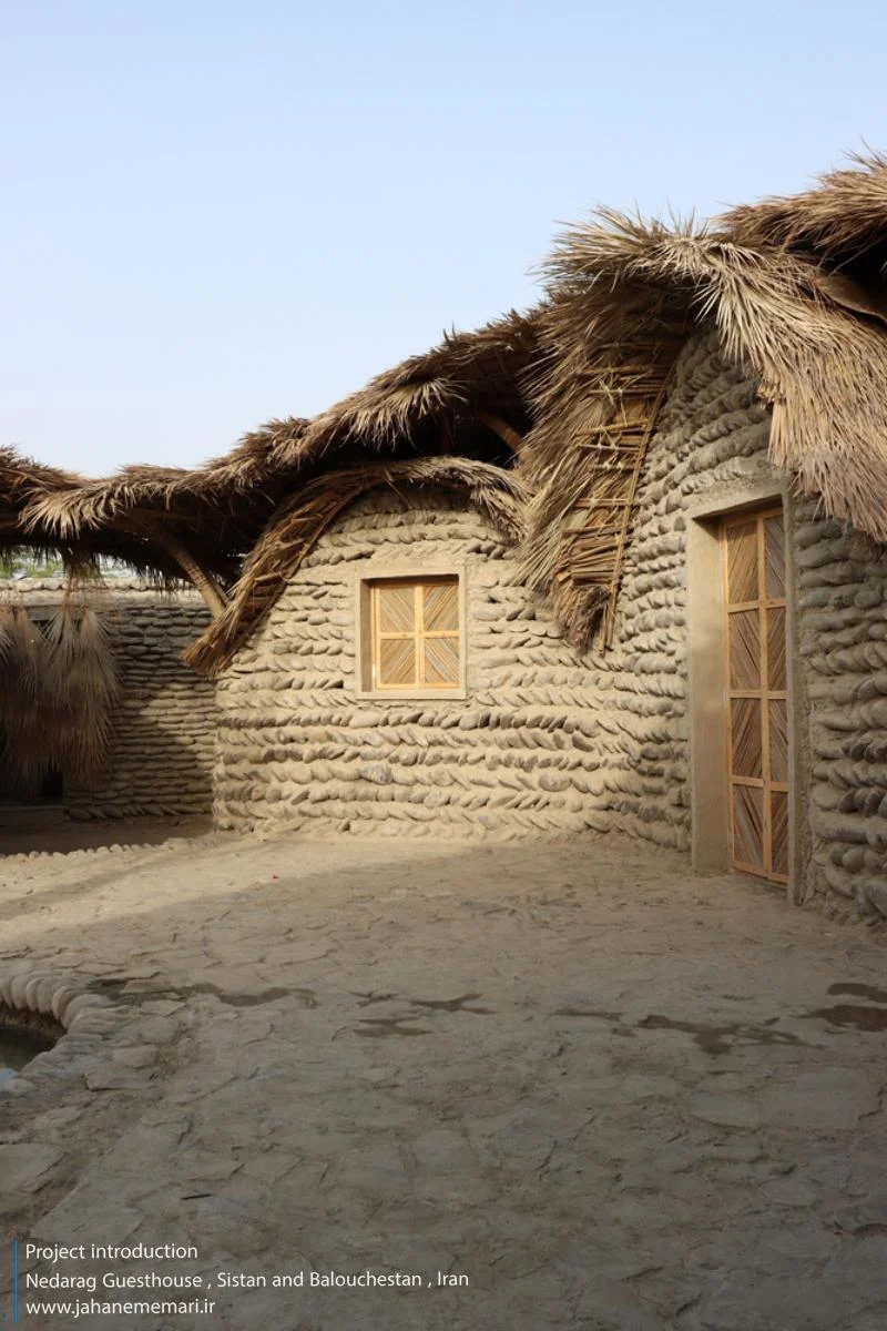 نمای خارجی و داخلی مهمانسرای ندارگ در روستای کهنانیکش، سیستان و بلوچستان، که ساختار نیمه‌باز، سقف چتری‌شکل با خرپاهای دست‌ساز و دیوارهای ضخیم گلی آن بر اساس بازتفسیر معماری بومی «کپر» و با هدف خنک‌سازی طبیعی و مشارکت جمعی اهالی طراحی و اجرا شده است.